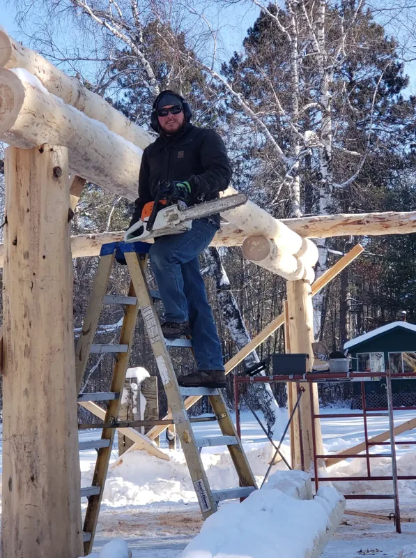 Worker repairing a cabin wall beside a stone chimney