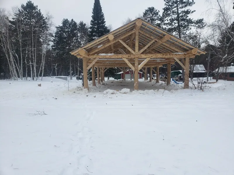 Open timber pavilion frame in a snowy clearing